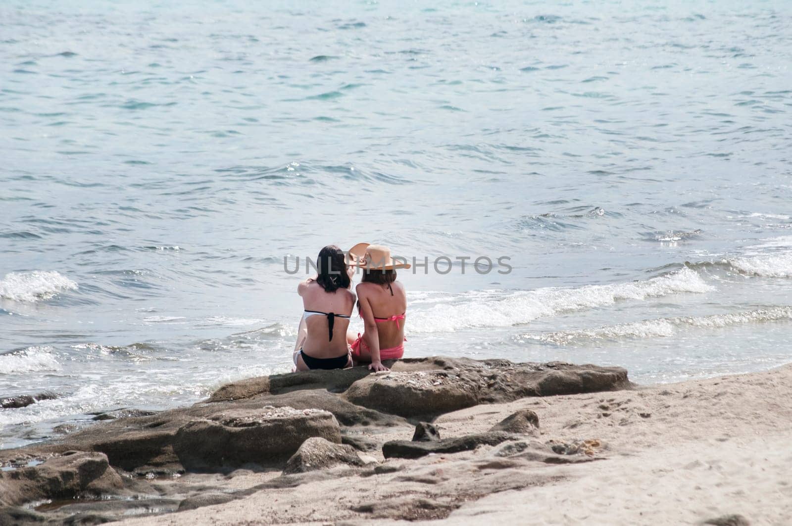 Two girls sitting back on sea beach rock