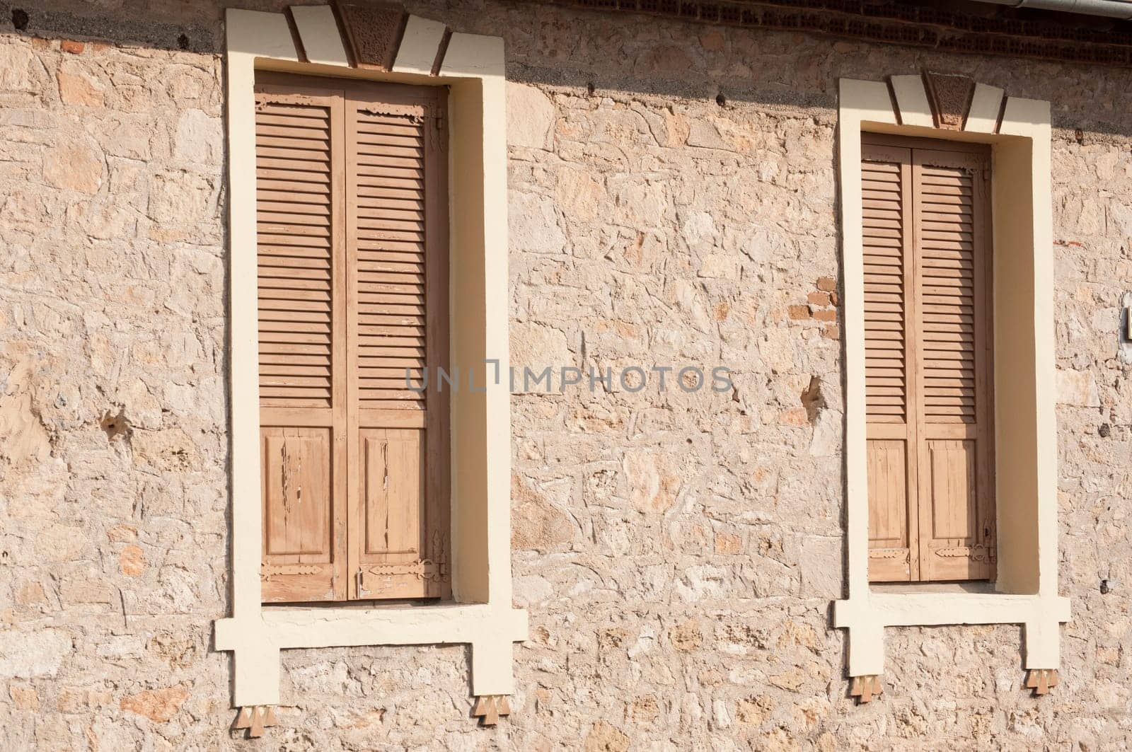 Two closed wooden windows on stone house wall