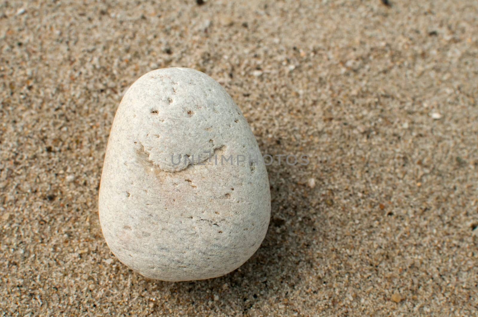 Naturally received image of smile on sea pebble stone on sand background