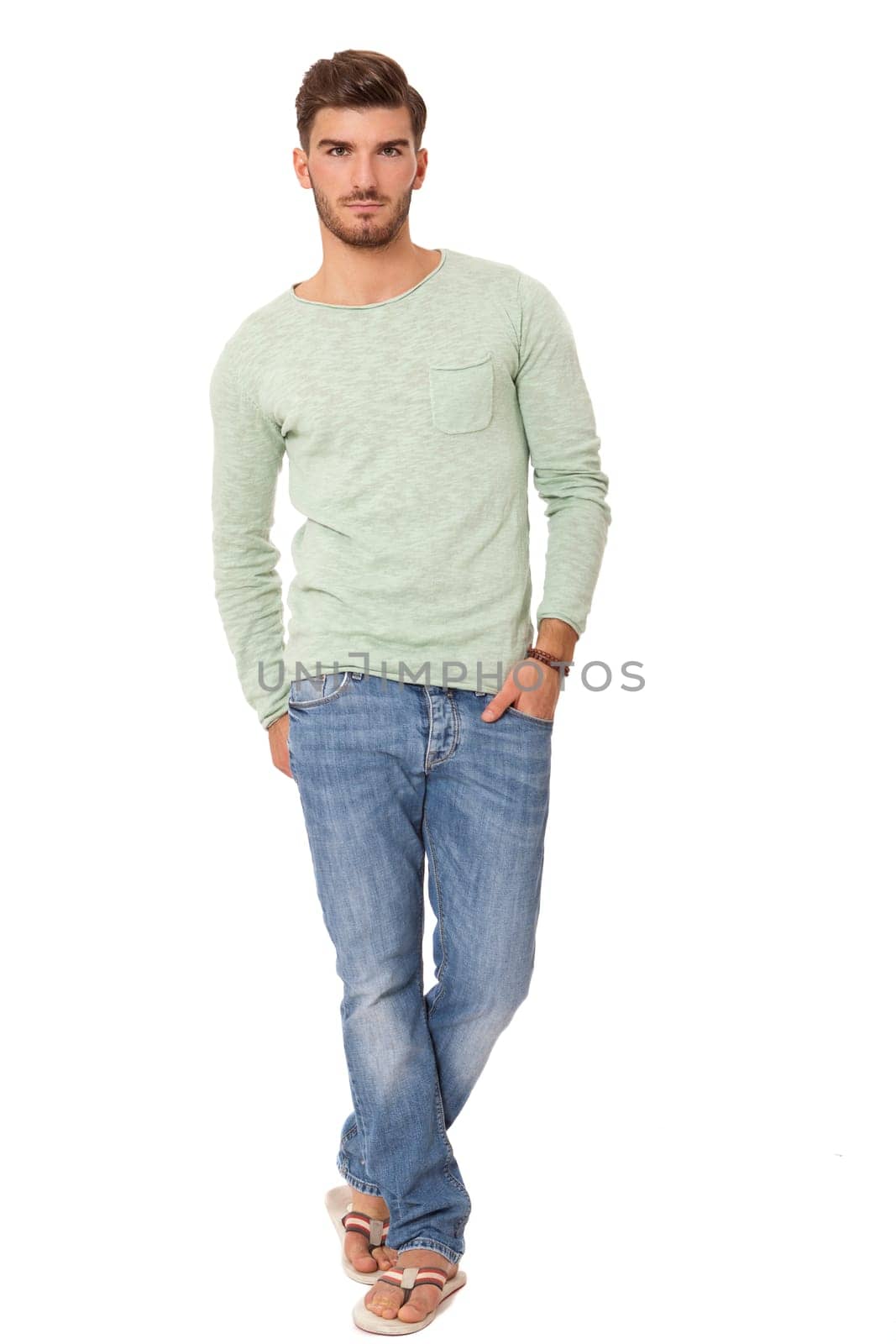 good-looking young man with beard posing with his hands in his pockets in jeans and sandals isolated on white background