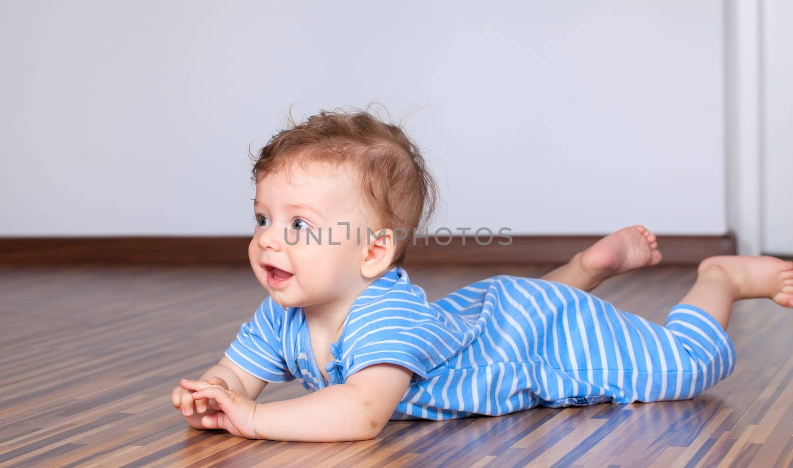 Portrait of a happy 6 months old baby boy crawling on wooden floor at home.