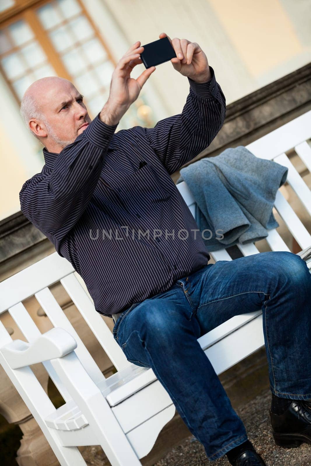 Attractive older man senior photographs himself with his mobile phone smartphone in the park
