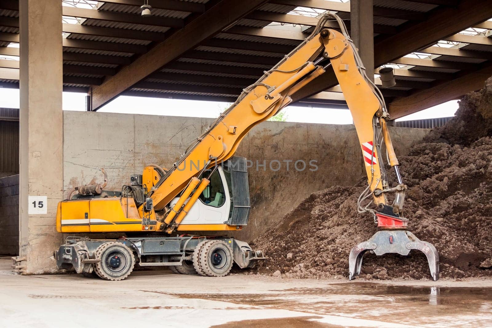 Excavator with gripper arm in front of a large pile of brown earth in the construction industry