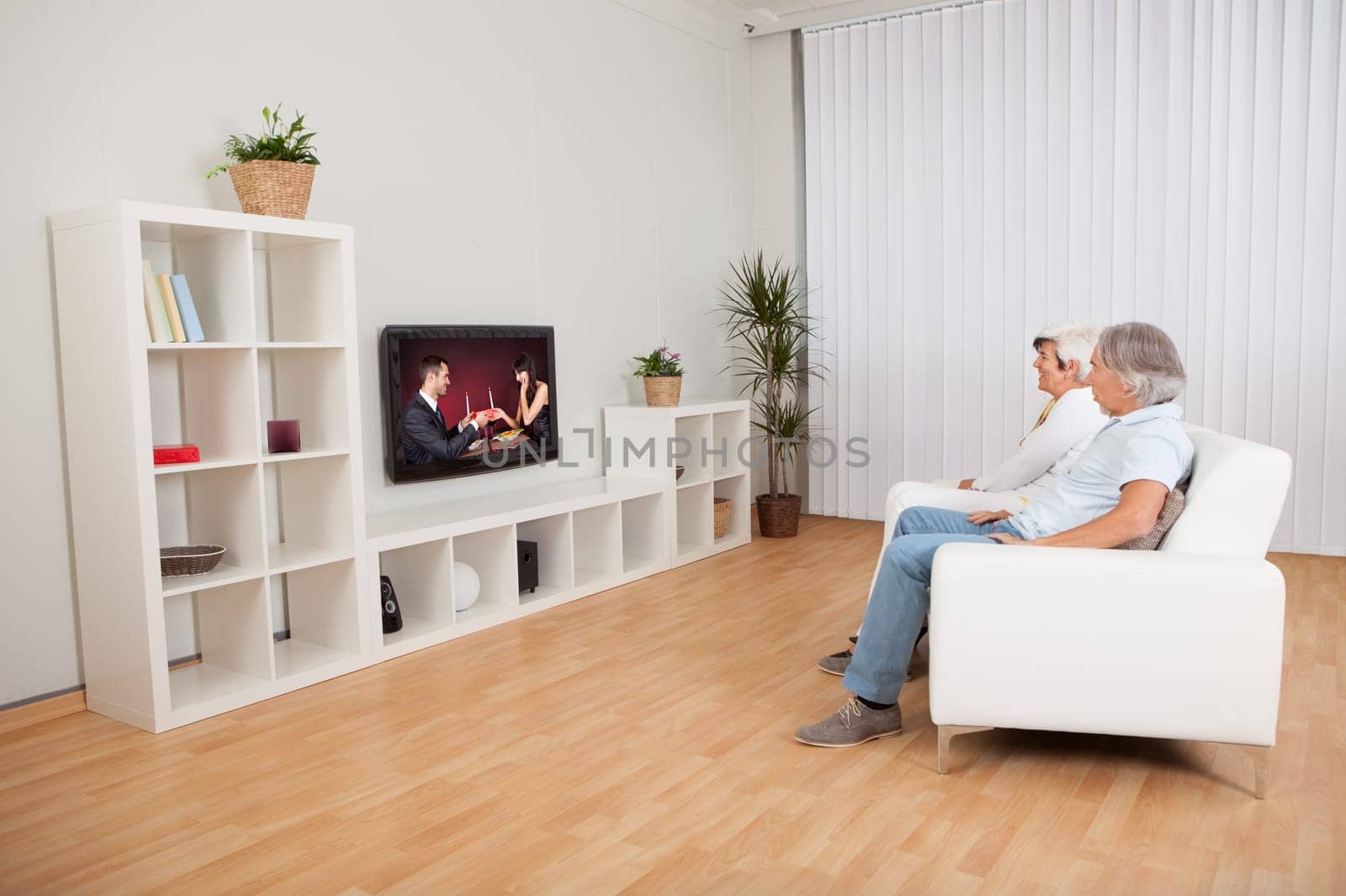 Rear view of a couple watching television with a scene on the screen of a young man and woman celebrating