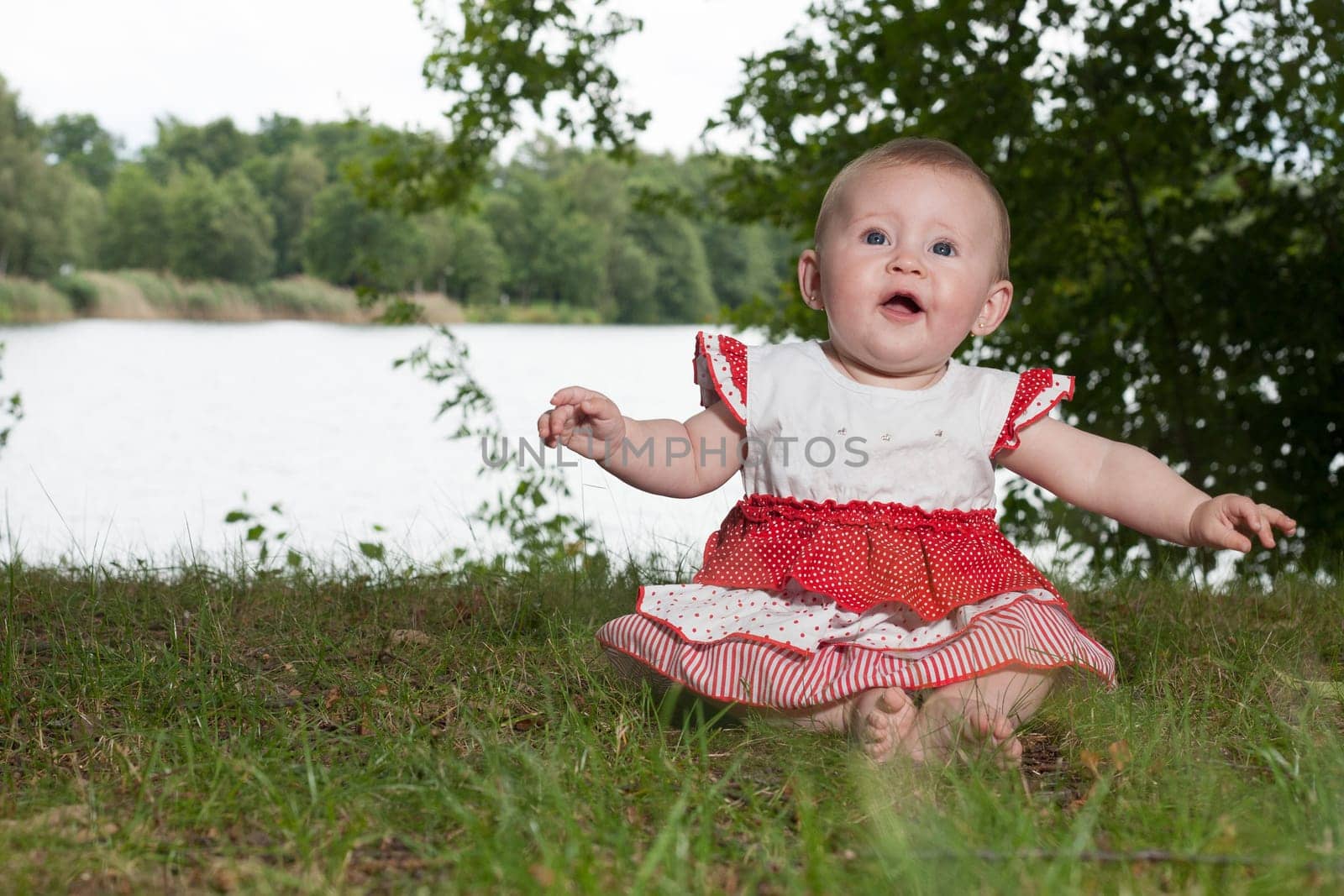 Little baby girl is sitting and playing near the lake