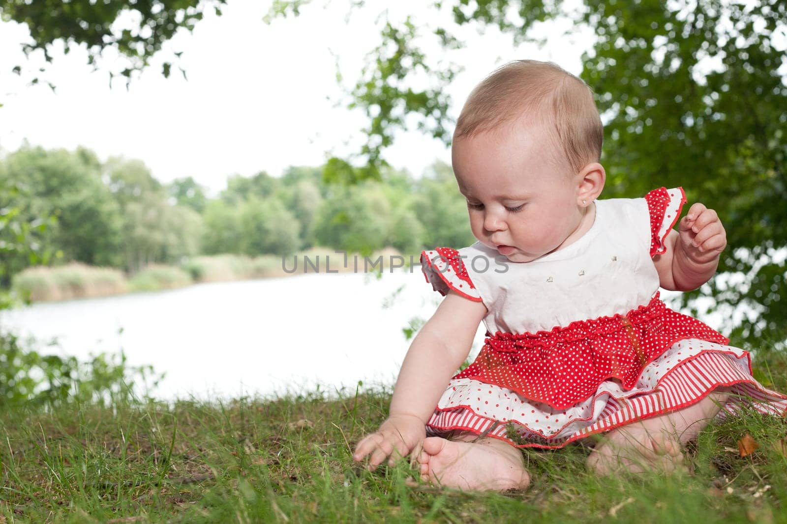 Little baby girl is sitting and playing near the lake