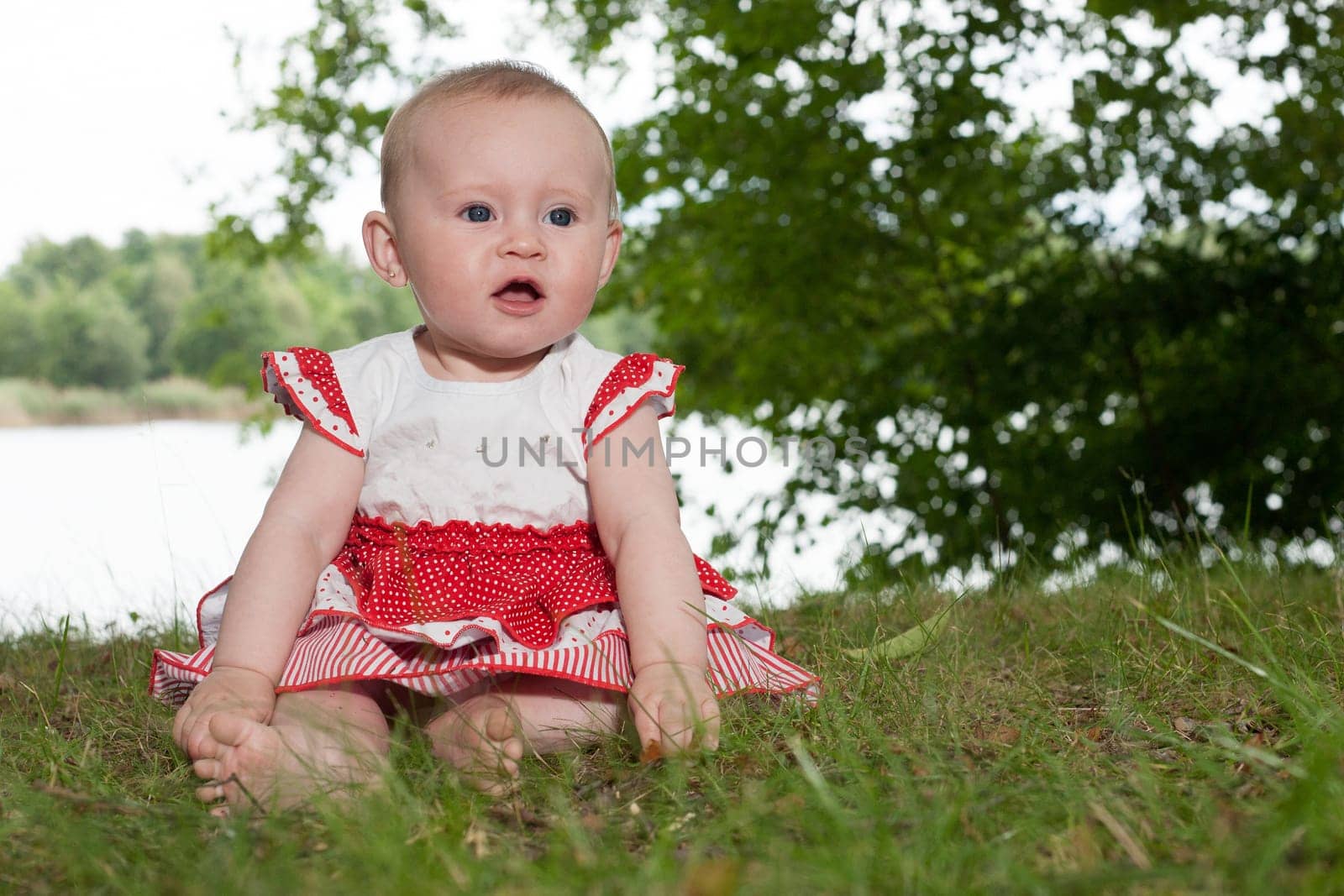 Little baby girl is sitting and playing near the lake