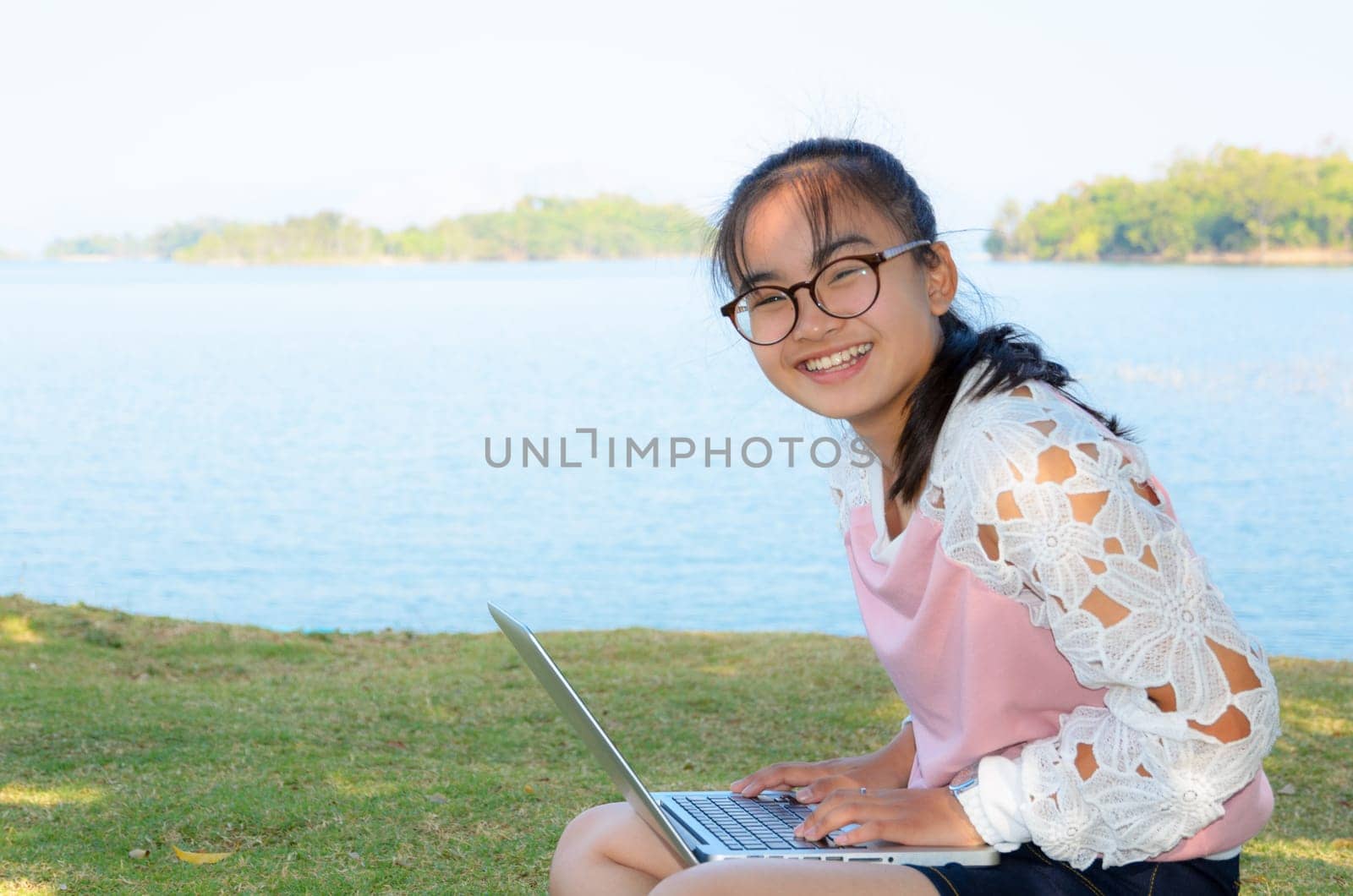 Young girl with laptop on the grass by the lake in park