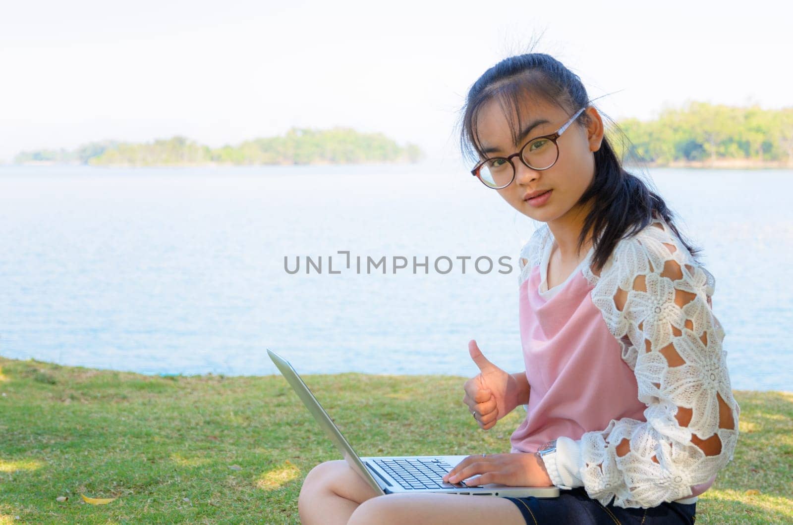 Young girl with laptop on the grass by the lake in park