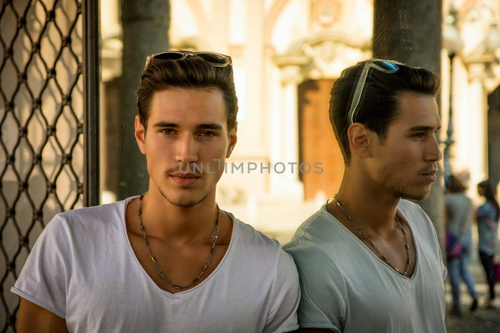 Handsome young man and his reflection in shop window outdoors, casually dressed