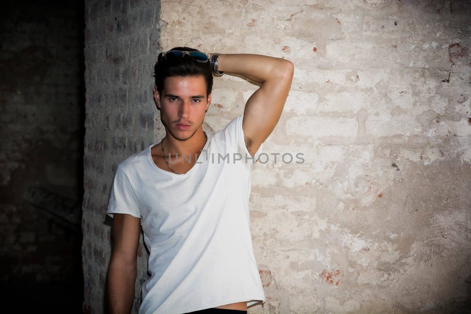 Handsome young man in old building against brick wall, looking at camera