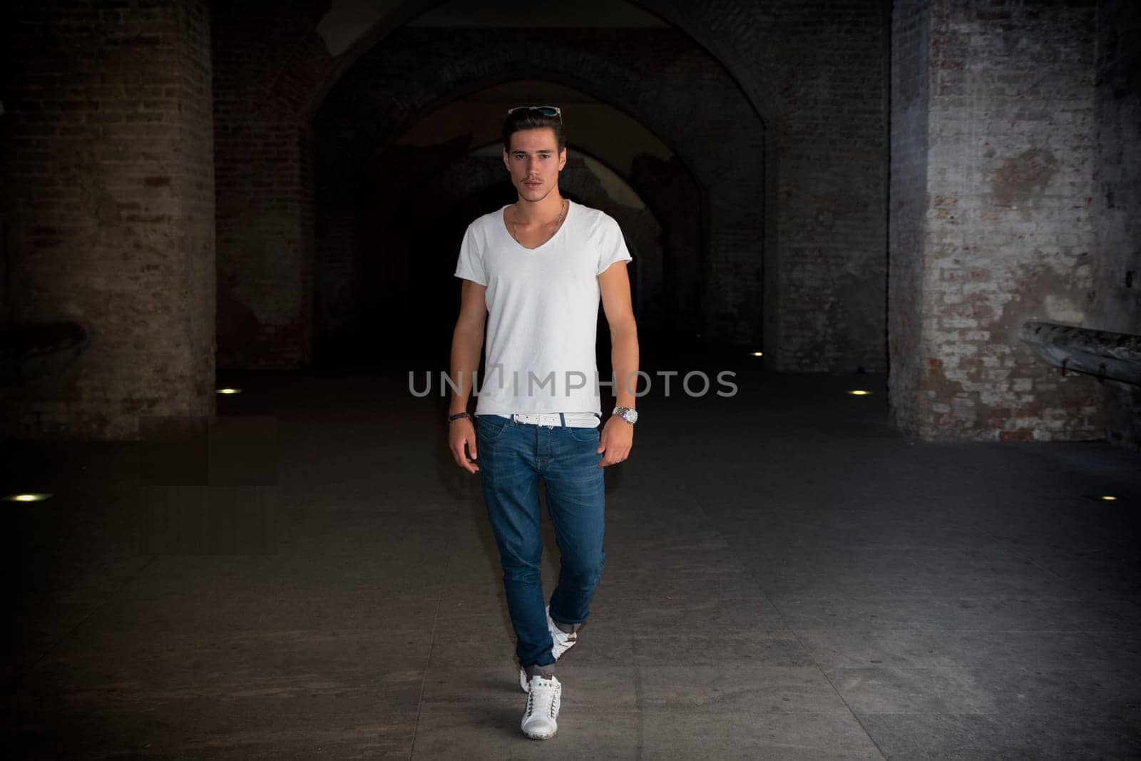 Handsome young man in old building walking inside gallery, looking at camera, full figure shot