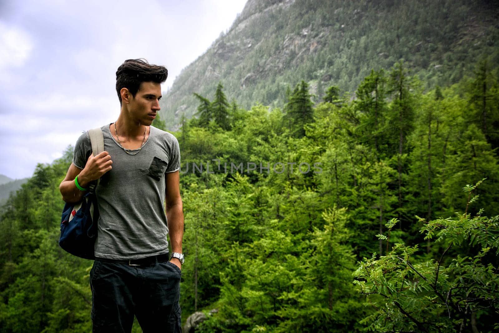 Handsome muscular young man backpacking or hiking in lush green mountain scenery pausing to look at something  on the ground