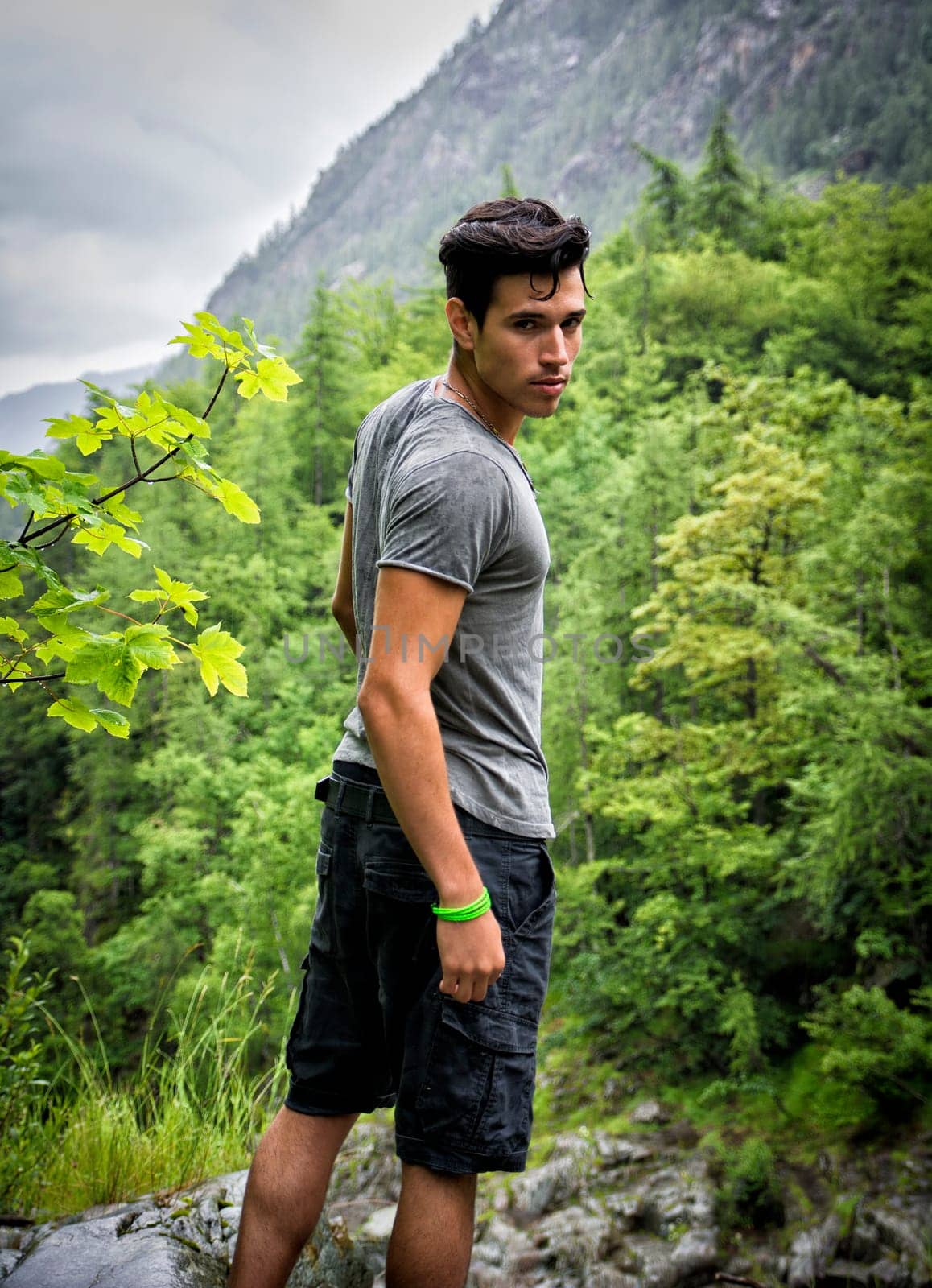 Handsome muscular young man hiking in lush green mountain scenery looking at camera