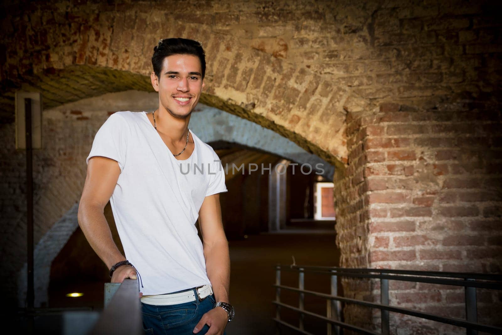 Handsome young man in old building leaning on handrail, smiling and looking at camera
