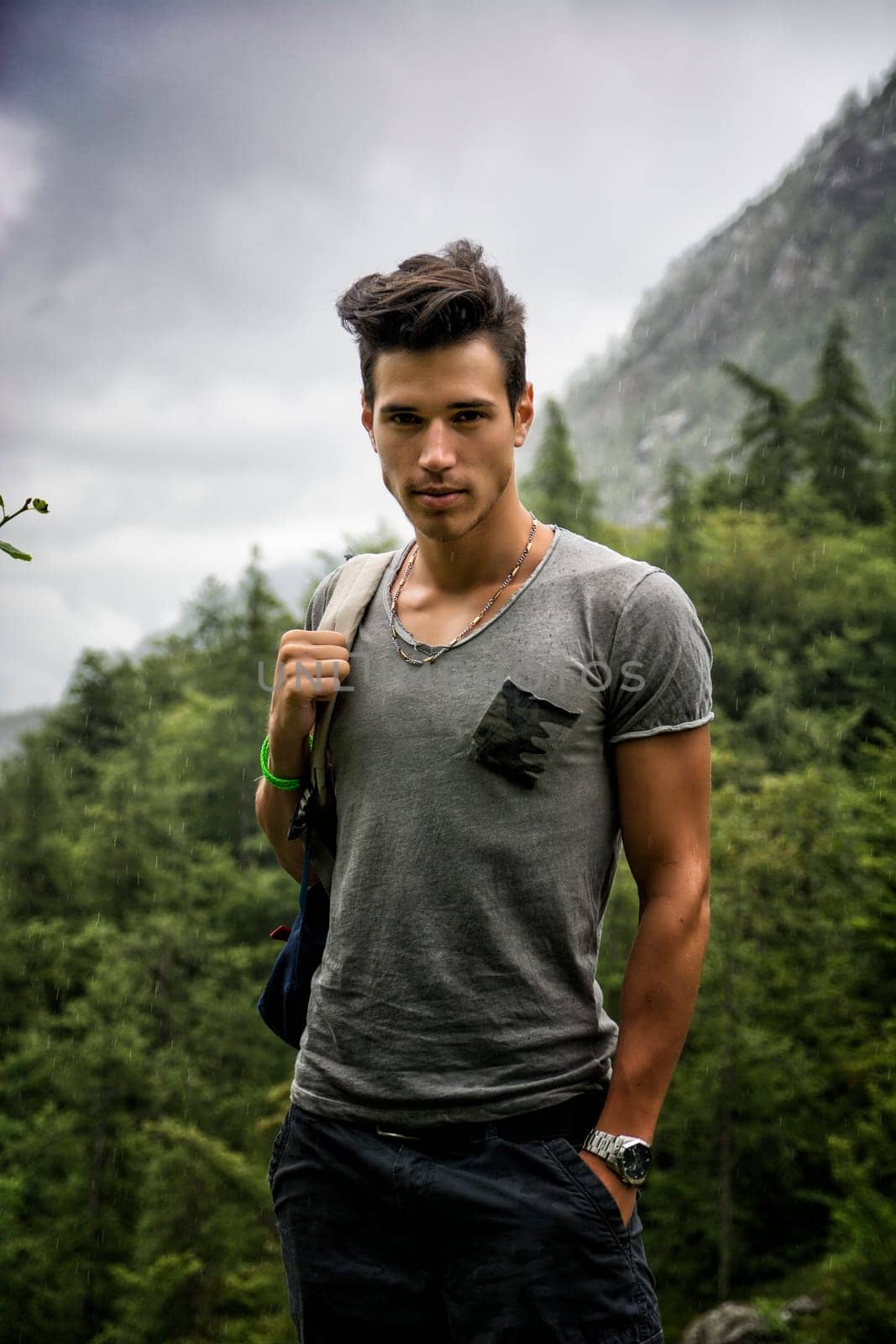 Handsome muscular young man backpacking or hiking in lush green mountain scenery looking at camera