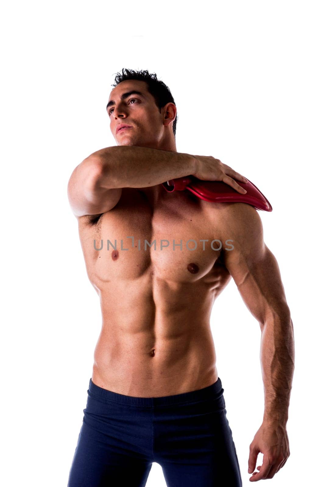 Muscular young man with shoulder pain, holding hot water bottle isolated on white