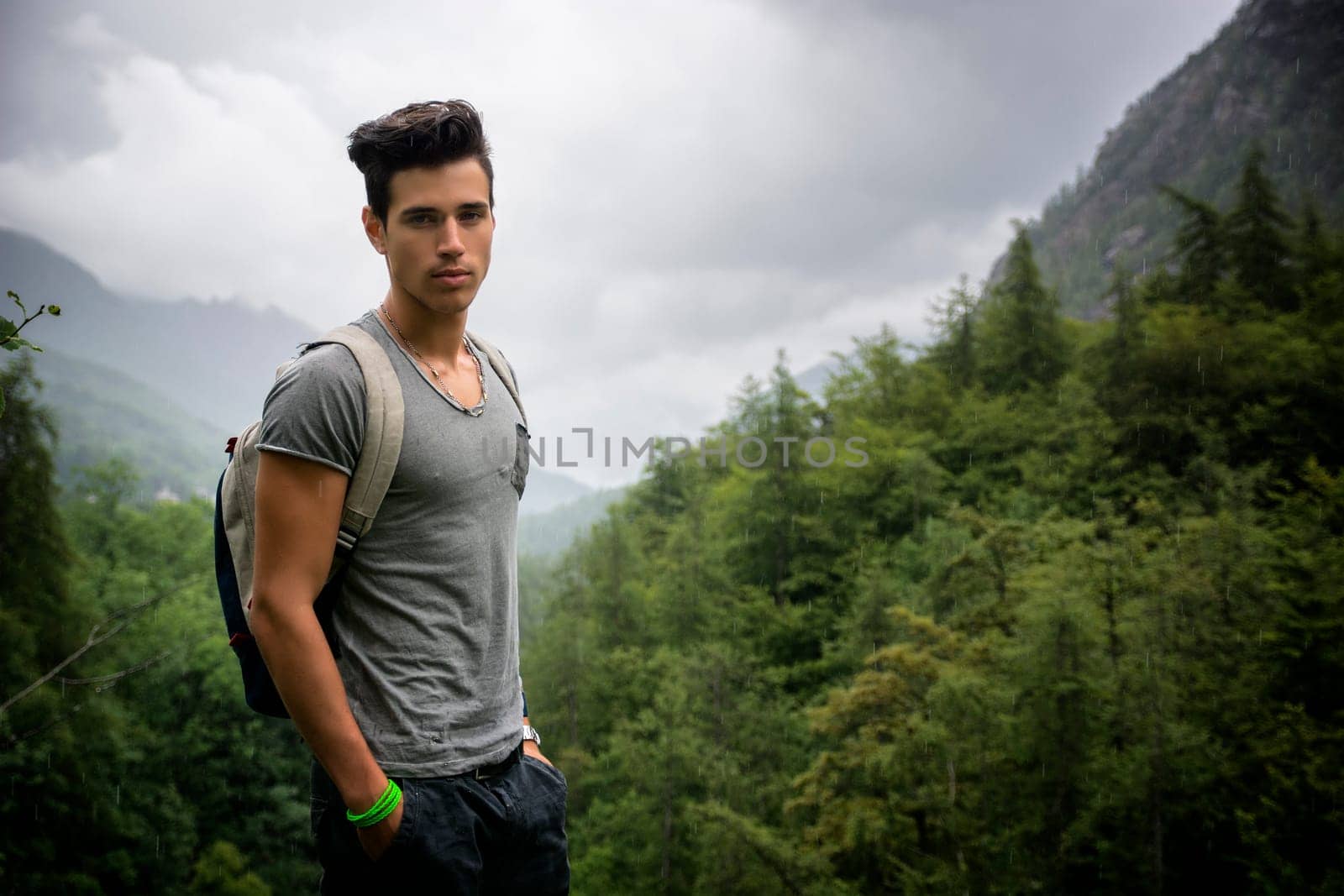 Handsome muscular young man backpacking or hiking in lush green mountain scenery looking at camera