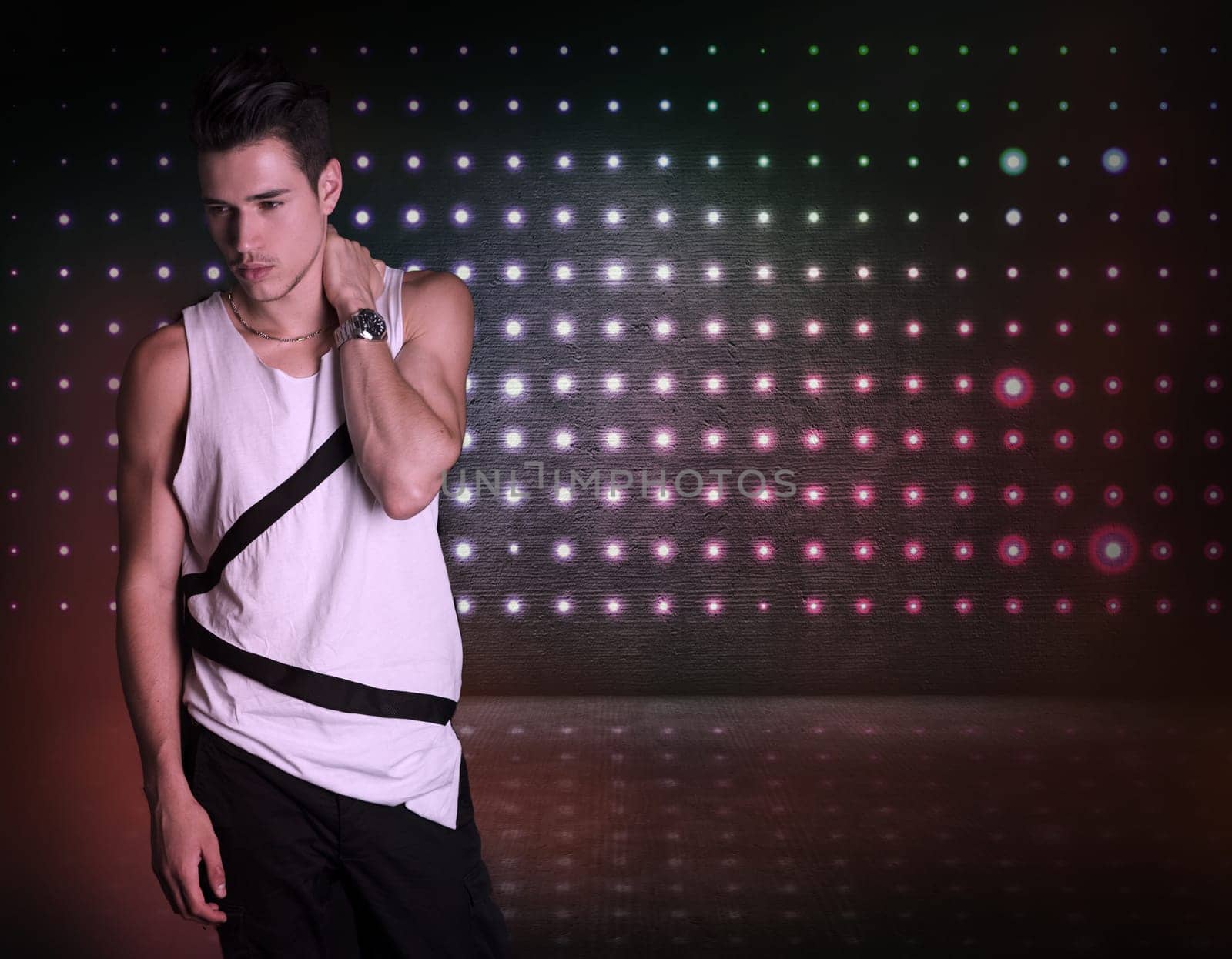 Hip young man standing on dark flashy background, looking to a side. Large copyspace