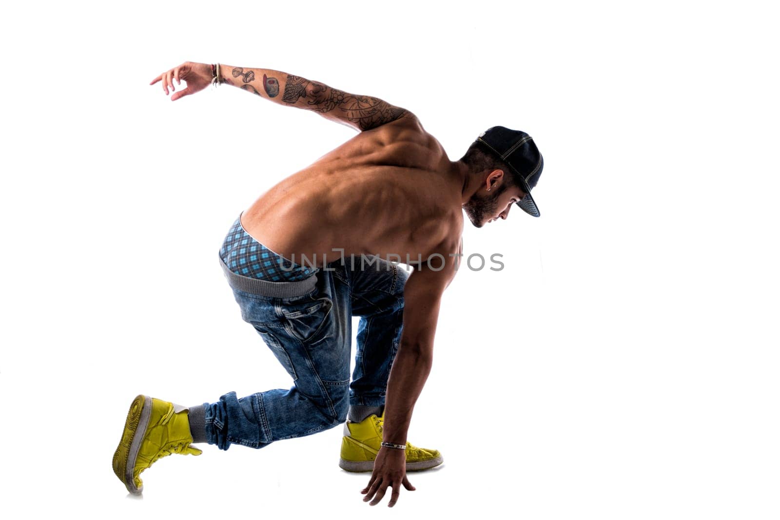 Athletic trendy shirtless young man in a hat doing a break dance routine isolated on white