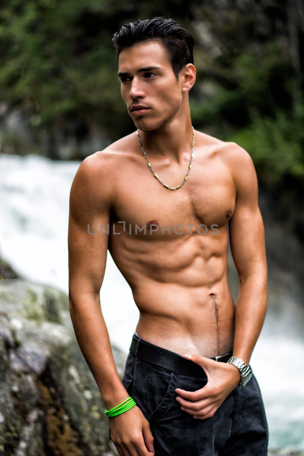 Handsome shirtless young man near mountain waterfall, with ripped fit body