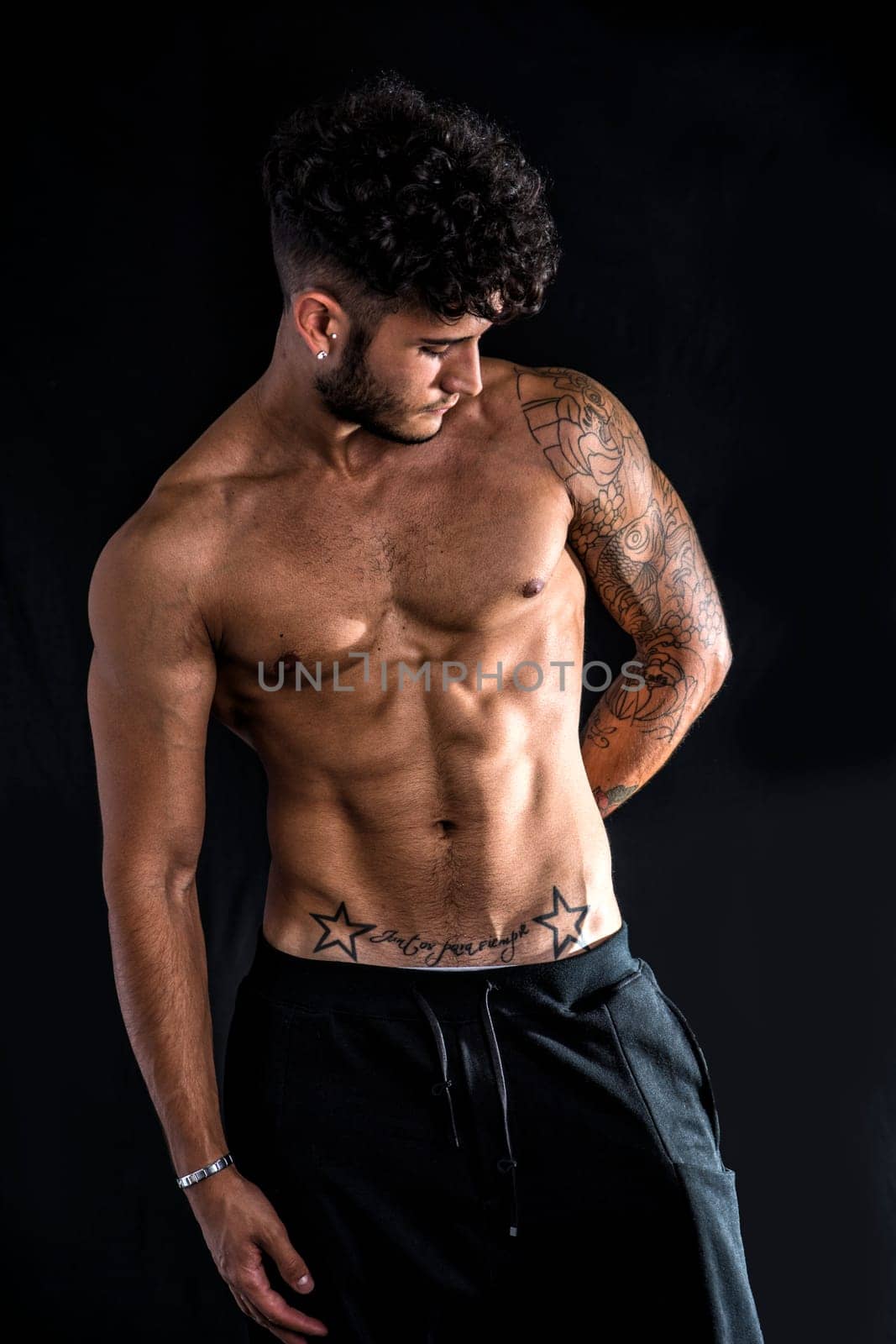 Young athletic man with tattoo posing isolated over black background, studio shot