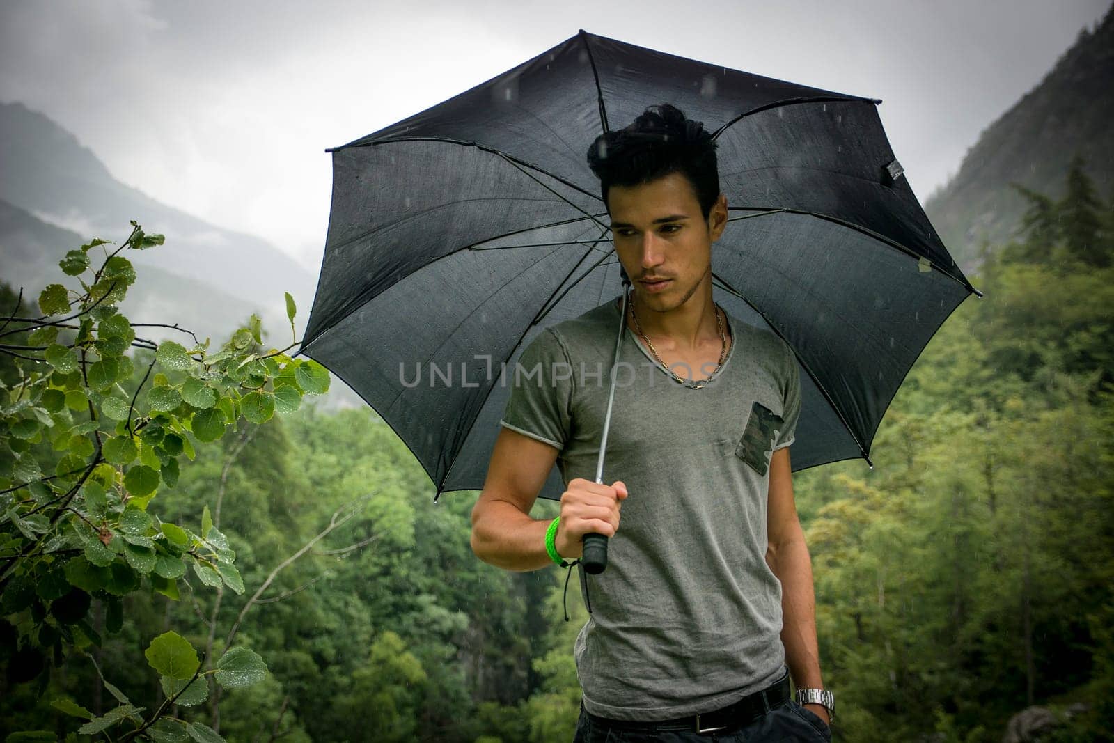 Smiling handsome young man holding an umbrella on a stormy day as he takes a walk along a trail in the mountains