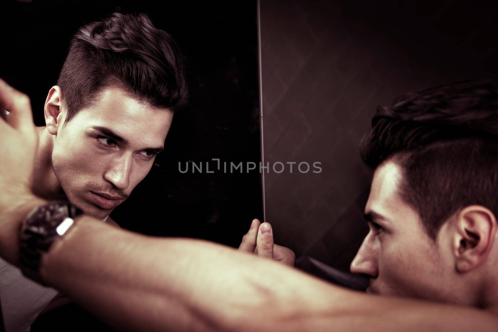 Narcissistic handsome young man leaning forwards admiring his reflection in the mirror in a show of self-absorption