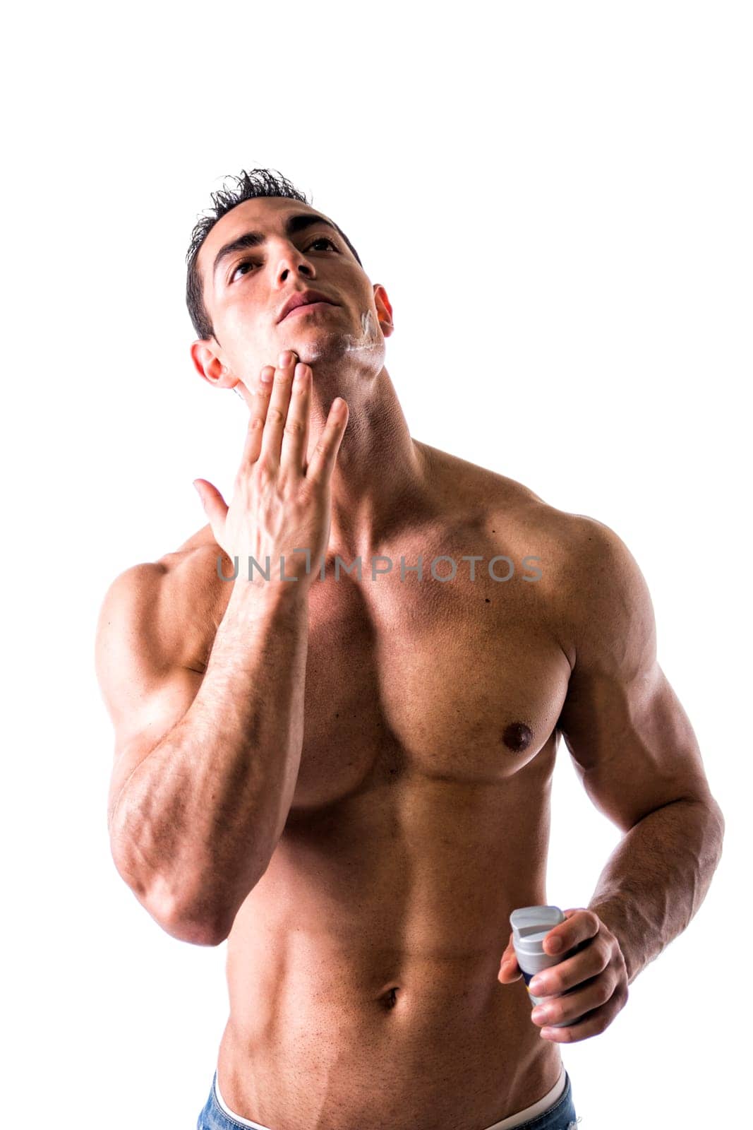 Man with muscular chest and abs applying shaving cream on his face on white background