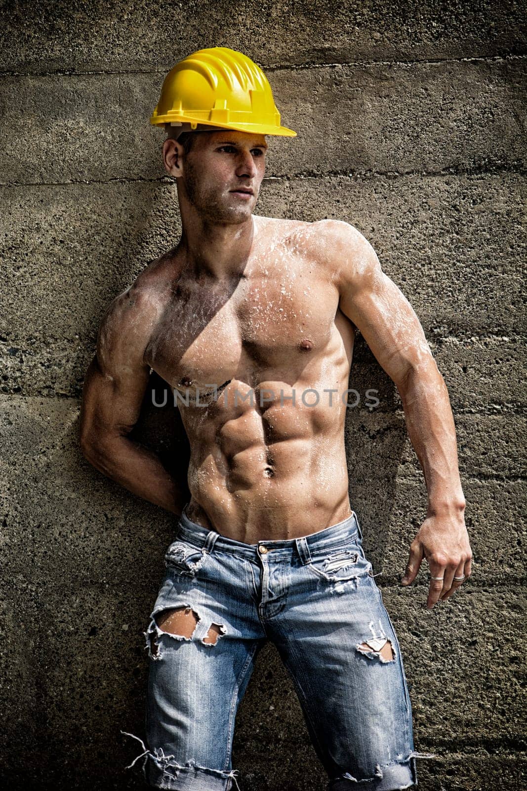 Handsome construction worker standing shirtless in front of a concrete wall