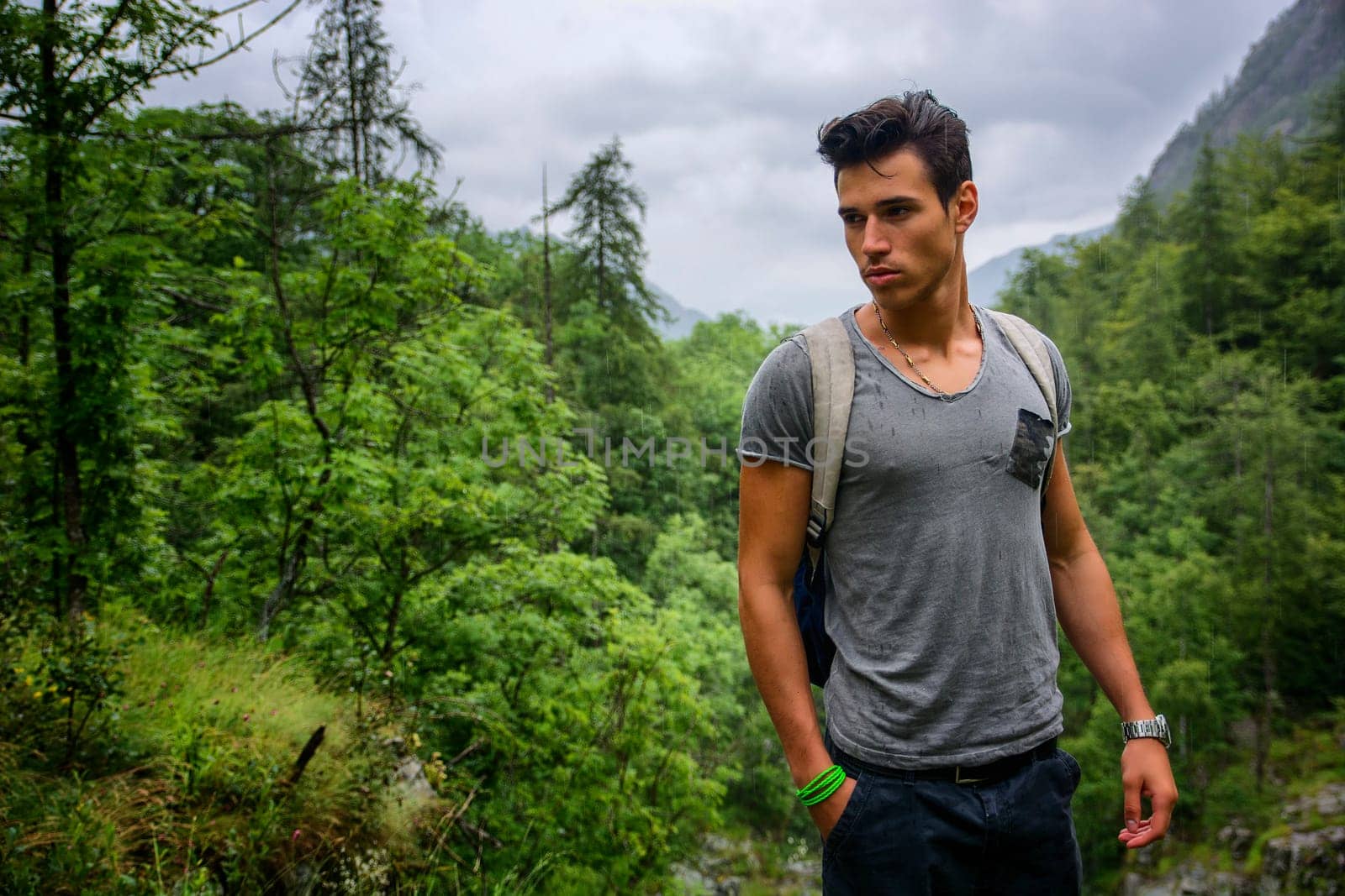 Handsome muscular young man backpacking or hiking in lush green mountain scenery pausing to look at something on the ground