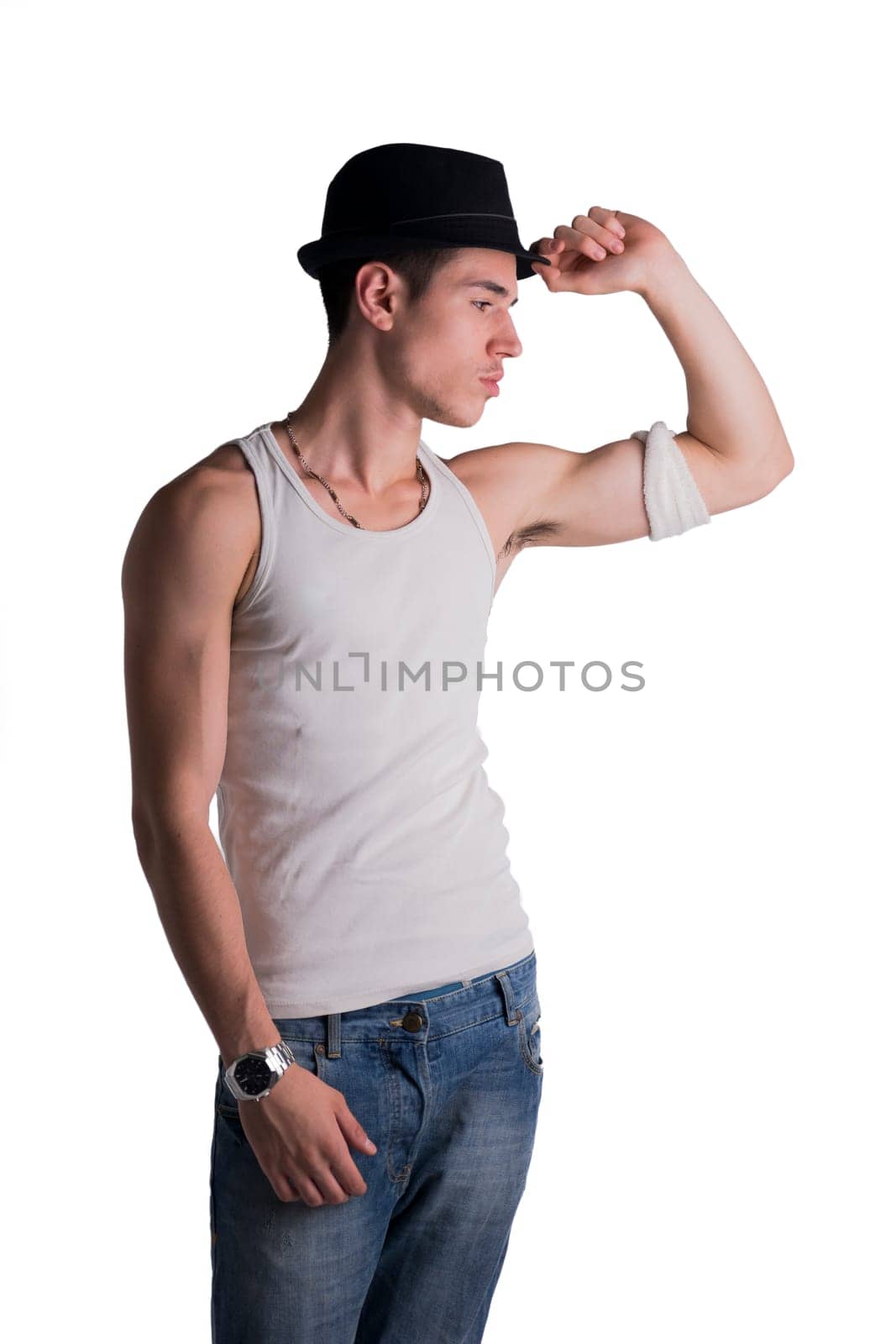 Trendy thoughtful man wearing a fashionable hat and tank top standing on white background, staring pensively at the floor