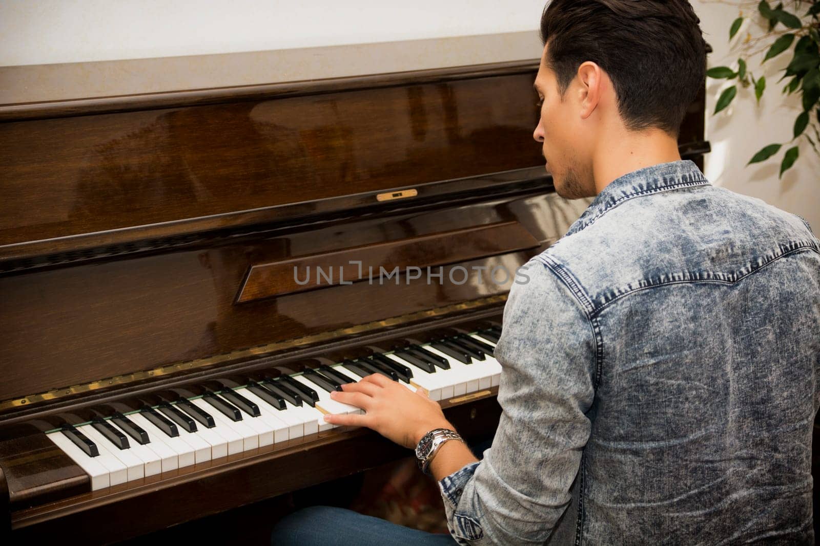 Young handsome male artist playing his wooden classical upright piano, indoor portrait