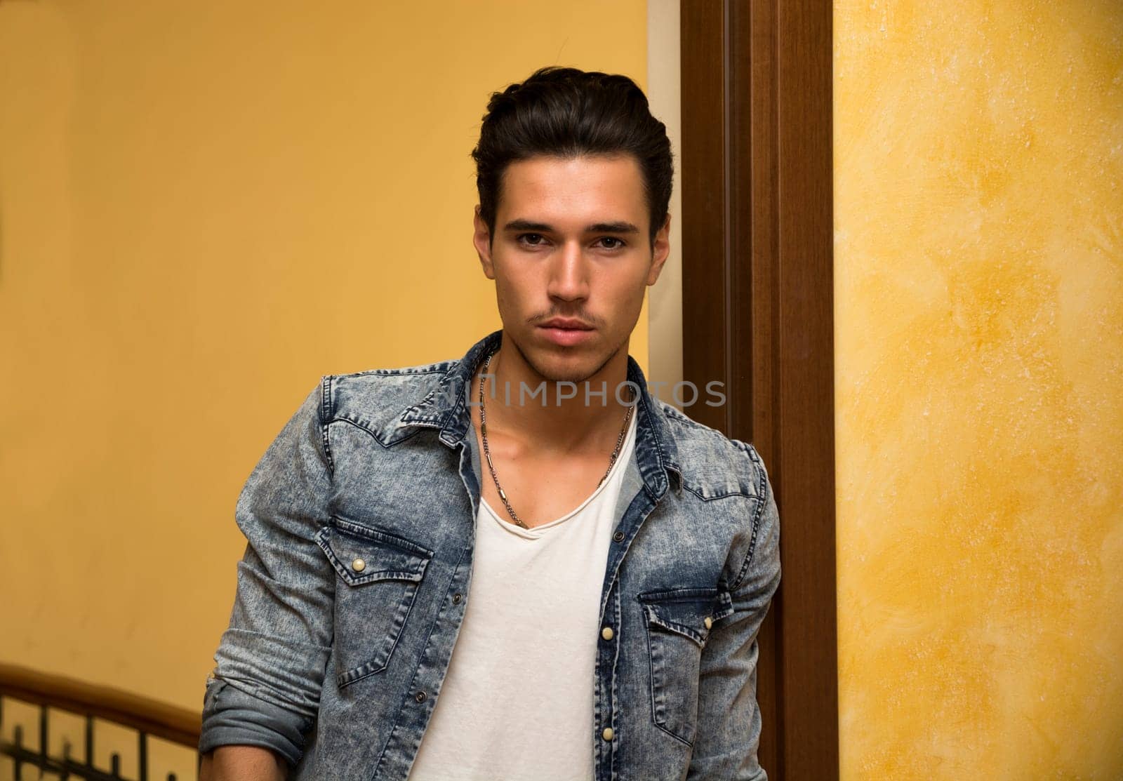 Attractive young man indoors, leaning against door jamb looking at camera