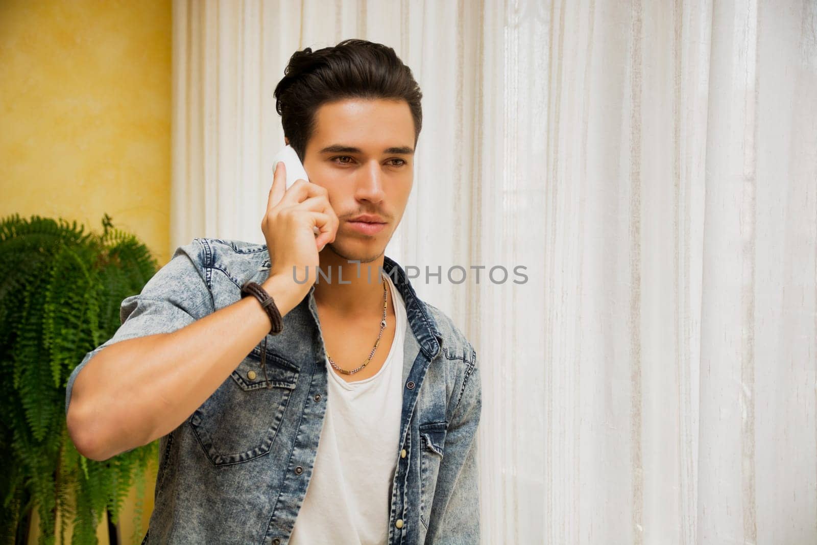 Handsome young man talking on telephone at home, looking to a side