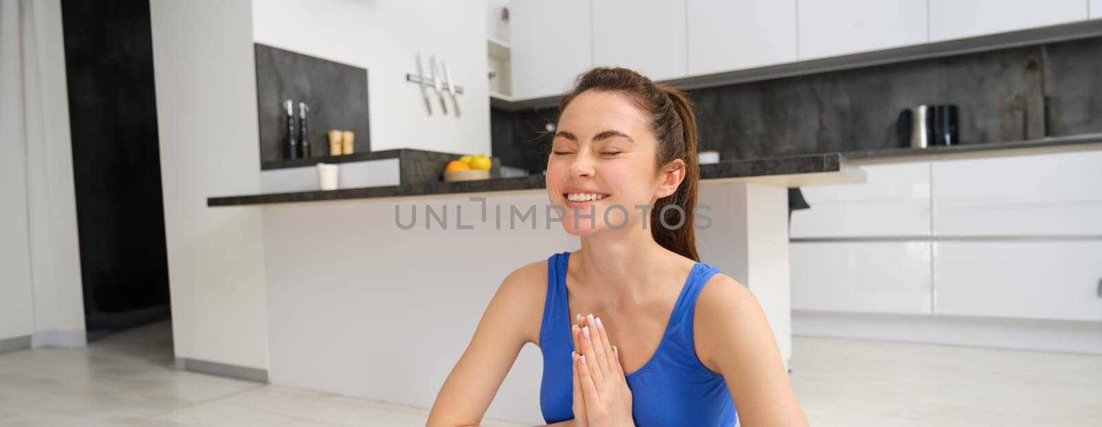 Image of beautiful woman doing training, workout from home in living room, practice yoga, sitting on floor and meditating.