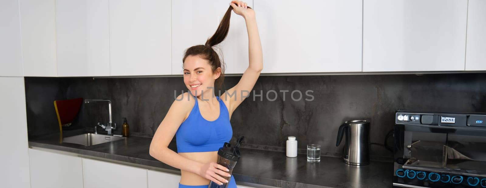Portrait of smiling, beautiful young woman drinking water and dietary supplement, taking vitamins after workout, showing her strong, healthy and shiny hair.