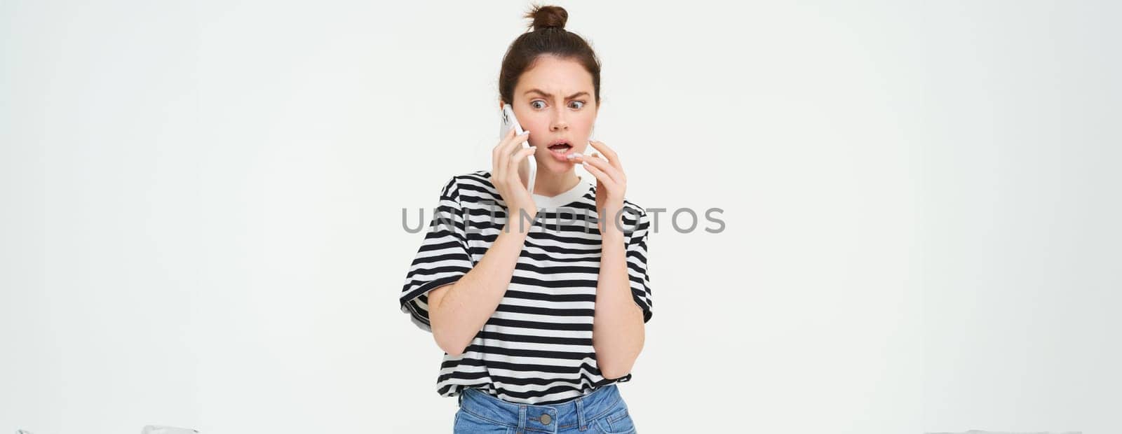 Image of woman with shocked face, looks confused while chats over the phone, listens to person on telephone, white background by Benzoix