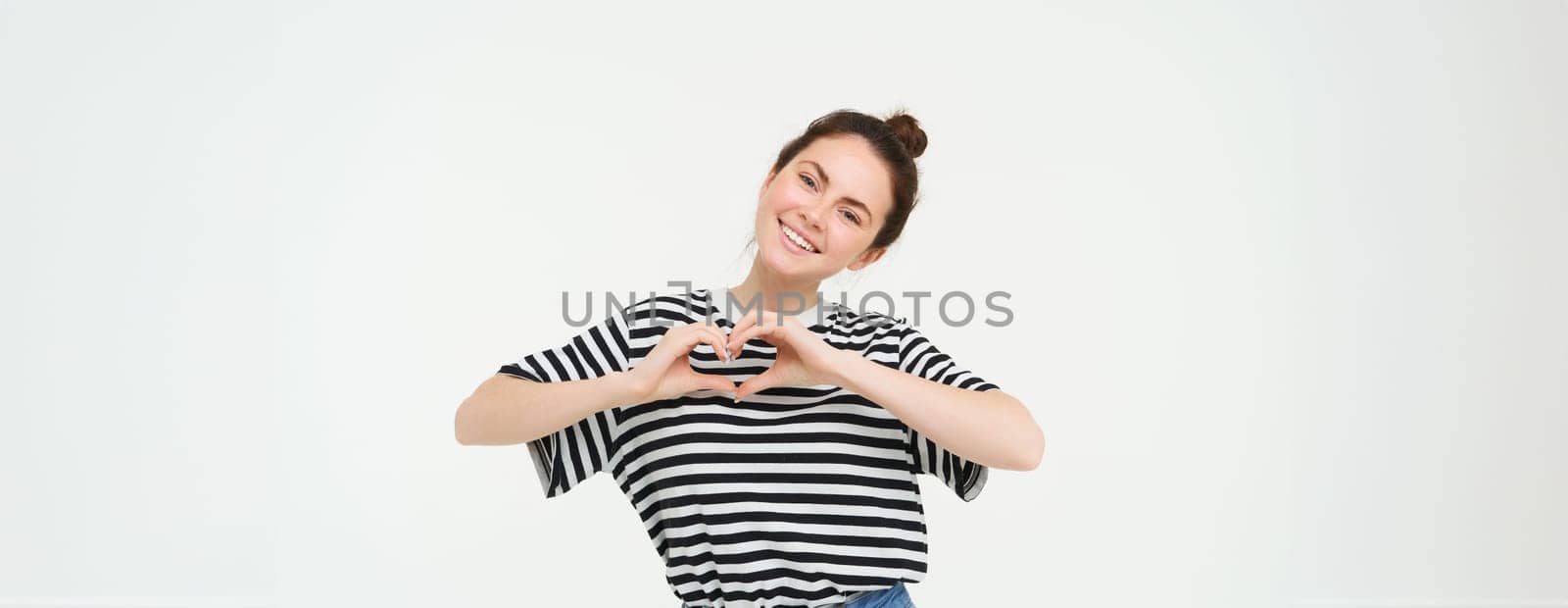 Beautiful european woman, shows heart sign, expresses her love and affection, flirting, standing over white background.