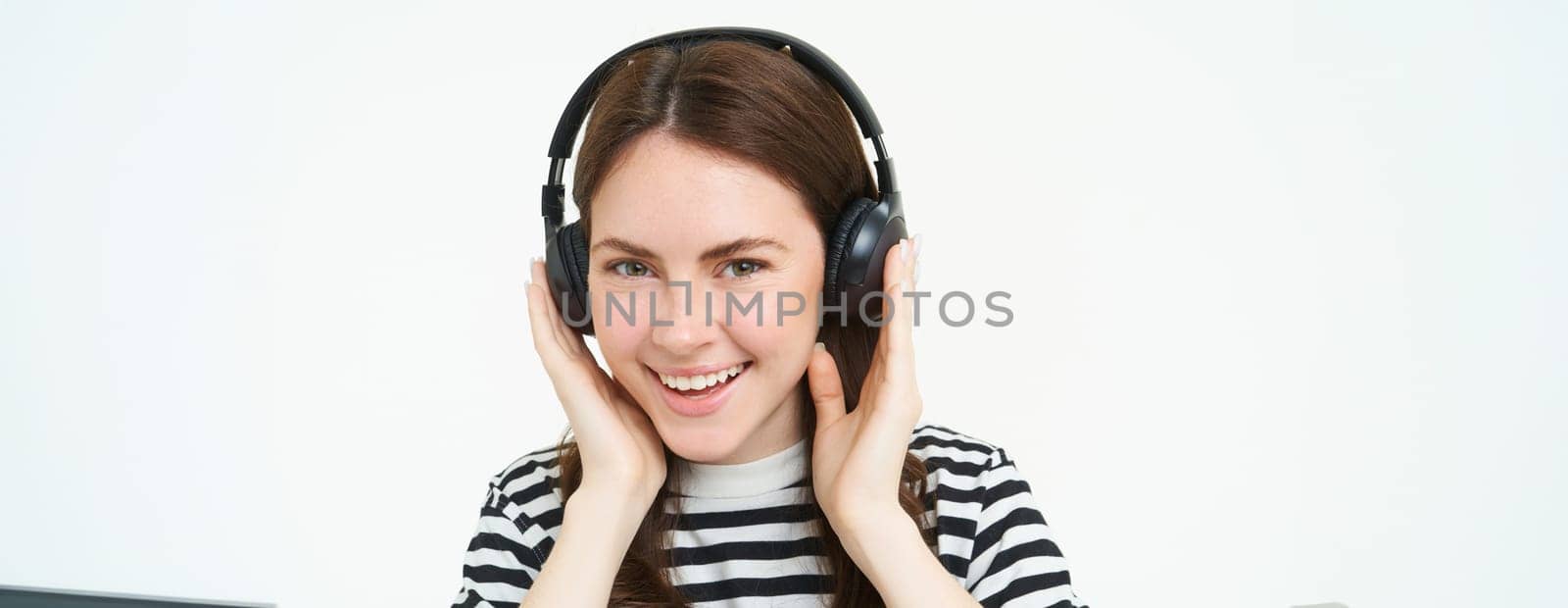 Portrait of woman, smiling, wearing wireless headphones, listening music, studying in earphones, standing isolated over white background.