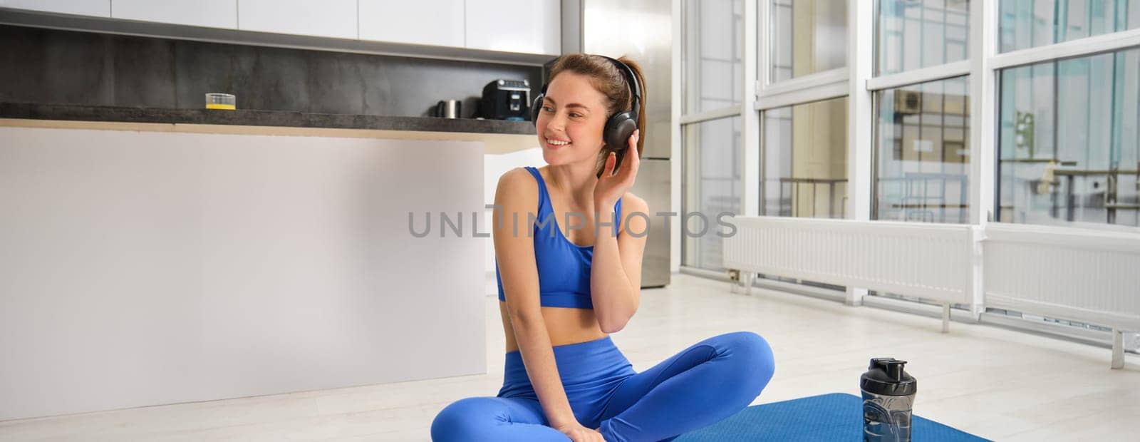 Portrait of woman in tracksuit, doing yoga training, workout at home with wireless headphones, listening music to focus.