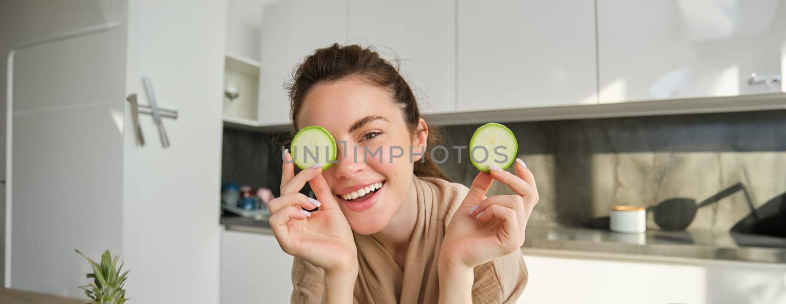 Portrait of beautiful brunette girl cooking in the kitchen, posing in bathrobe at home, holding zucchini, showing happy smile, making healthy food, vegetarian meal.