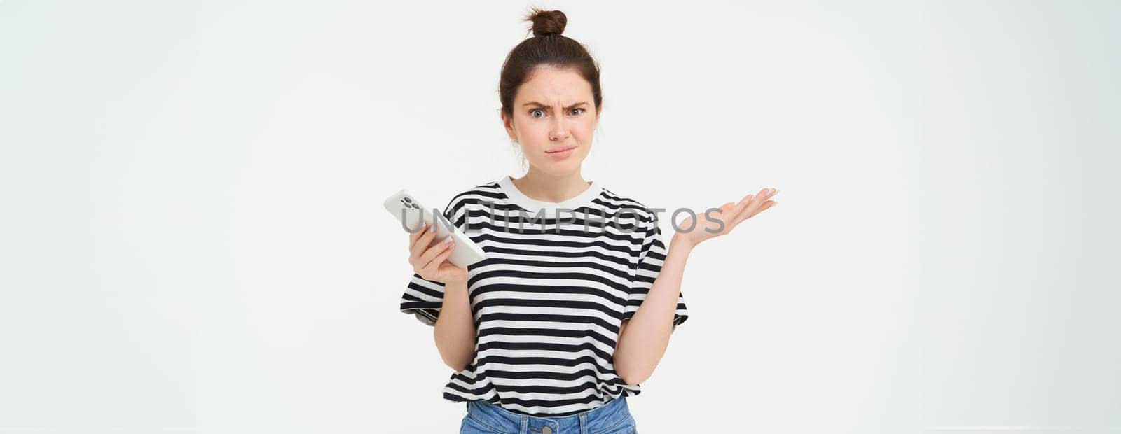 Confused woman shrugging shoulders, holds hands sideways, has phone in palm, clueless, frowning and looking puzzled, isolated over white background by Benzoix
