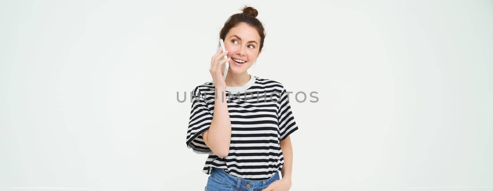 Happy young woman talks on mobile phone, chats on telephone, uses smartphone, stands over white background. Copy space