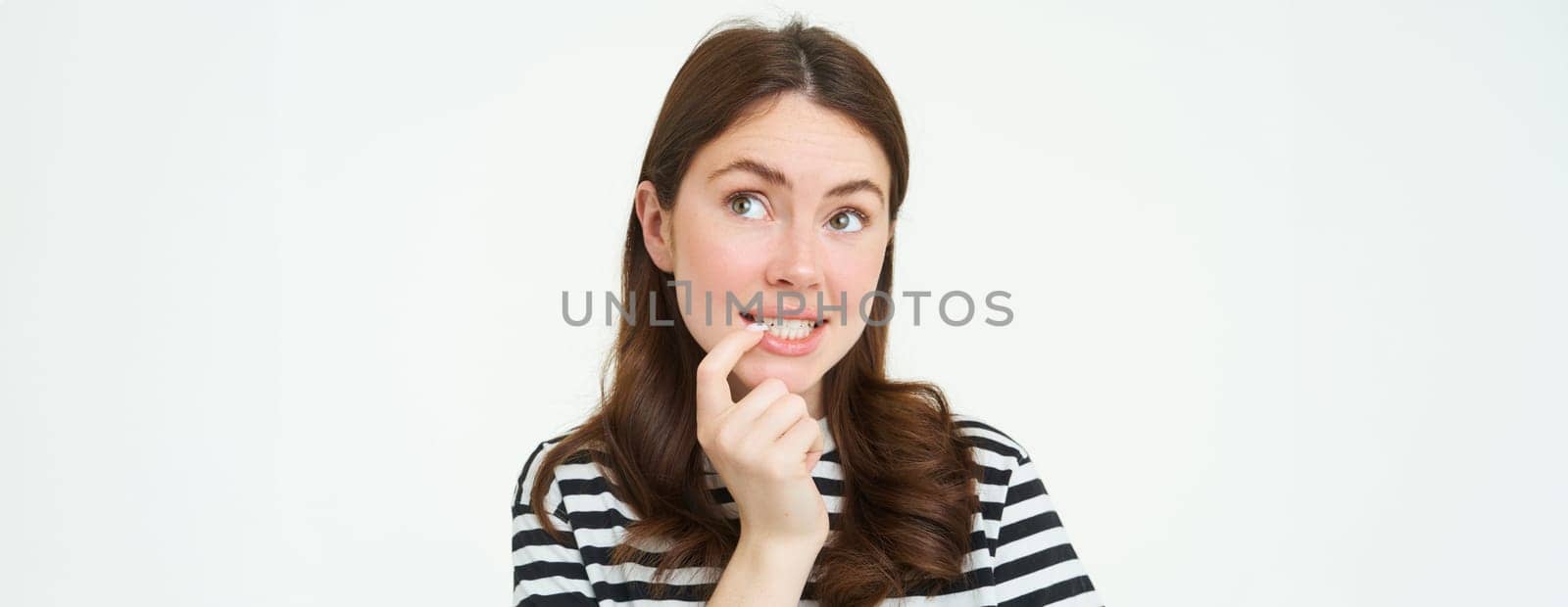 Portrait of curious young woman, bites her finger and looks up thoughtful, thinking, makes decision, choosing smth to eat, stands over white background.