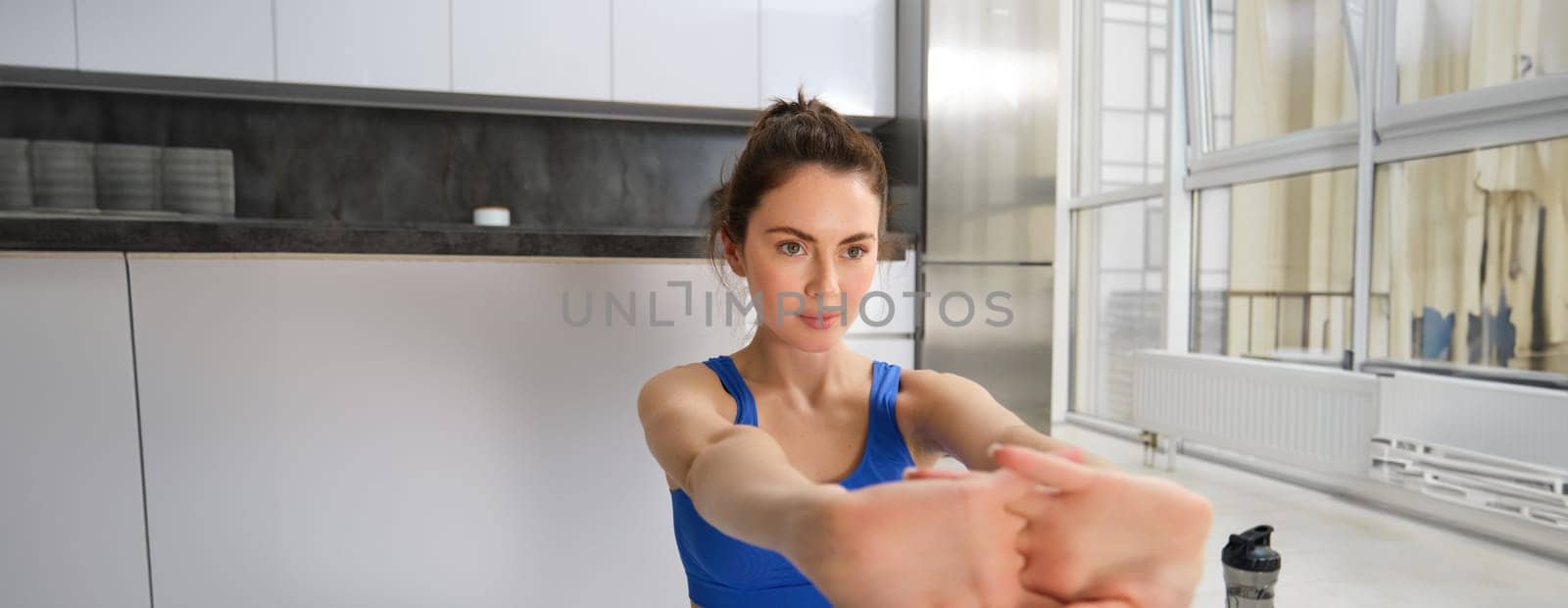 Close up portrait of active and healthy young woman, stretching her arms, workout from home, doing fitness exercises, aerobics training in living room, looking focused.