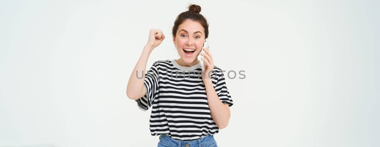 Enthusiastic young woman laughing, answers phone call and celebrating, receiving good news over the telephone, isolated over white background by Benzoix