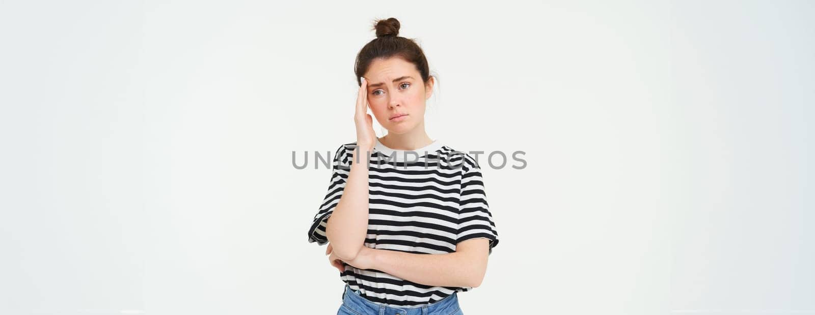 Portrait of concerned, worried young woman, touches her head, looking complicated, standing over white background.