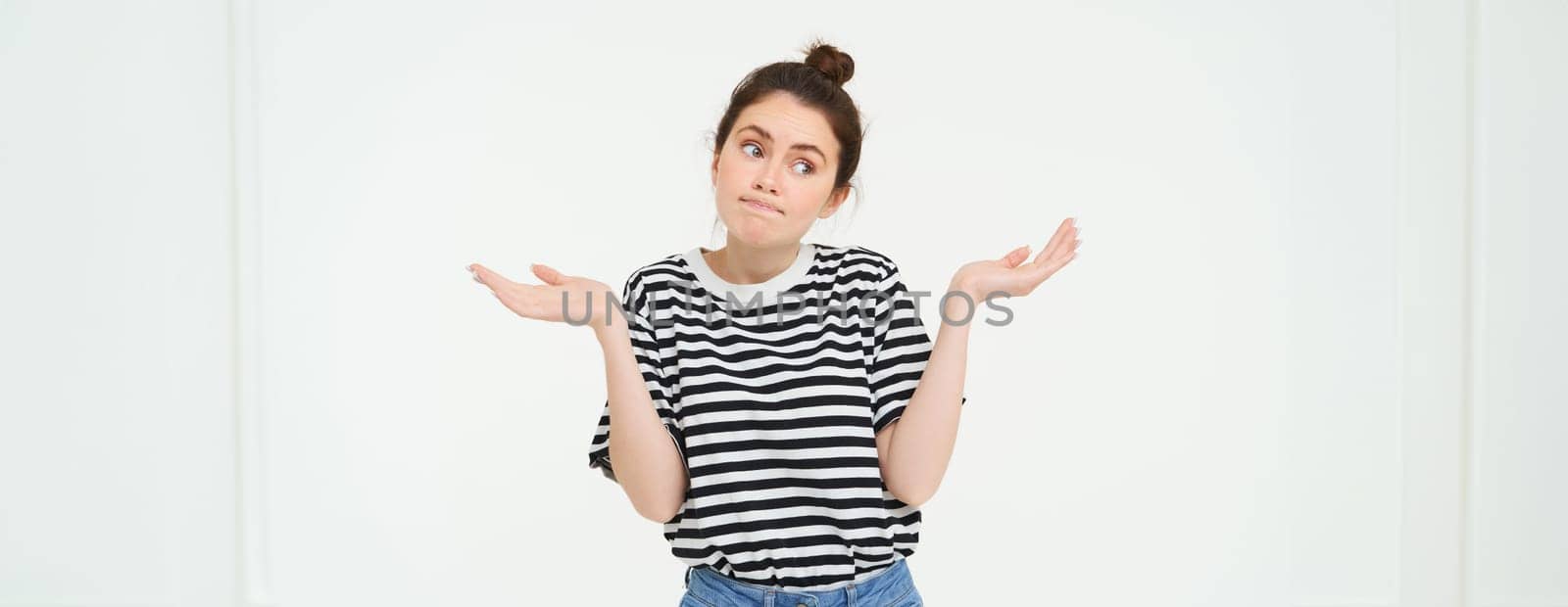 Image of confused brunette girl shrugging shoulders, looks puzzled, isolated over white background.