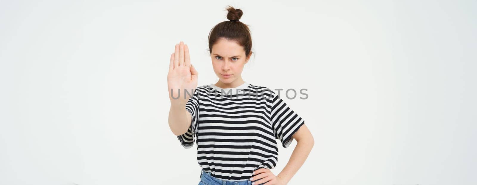 Image of woman frowning, showing one palm, stop gesture, disapprove and reject something, makes prohibit gesture, standing over white background.